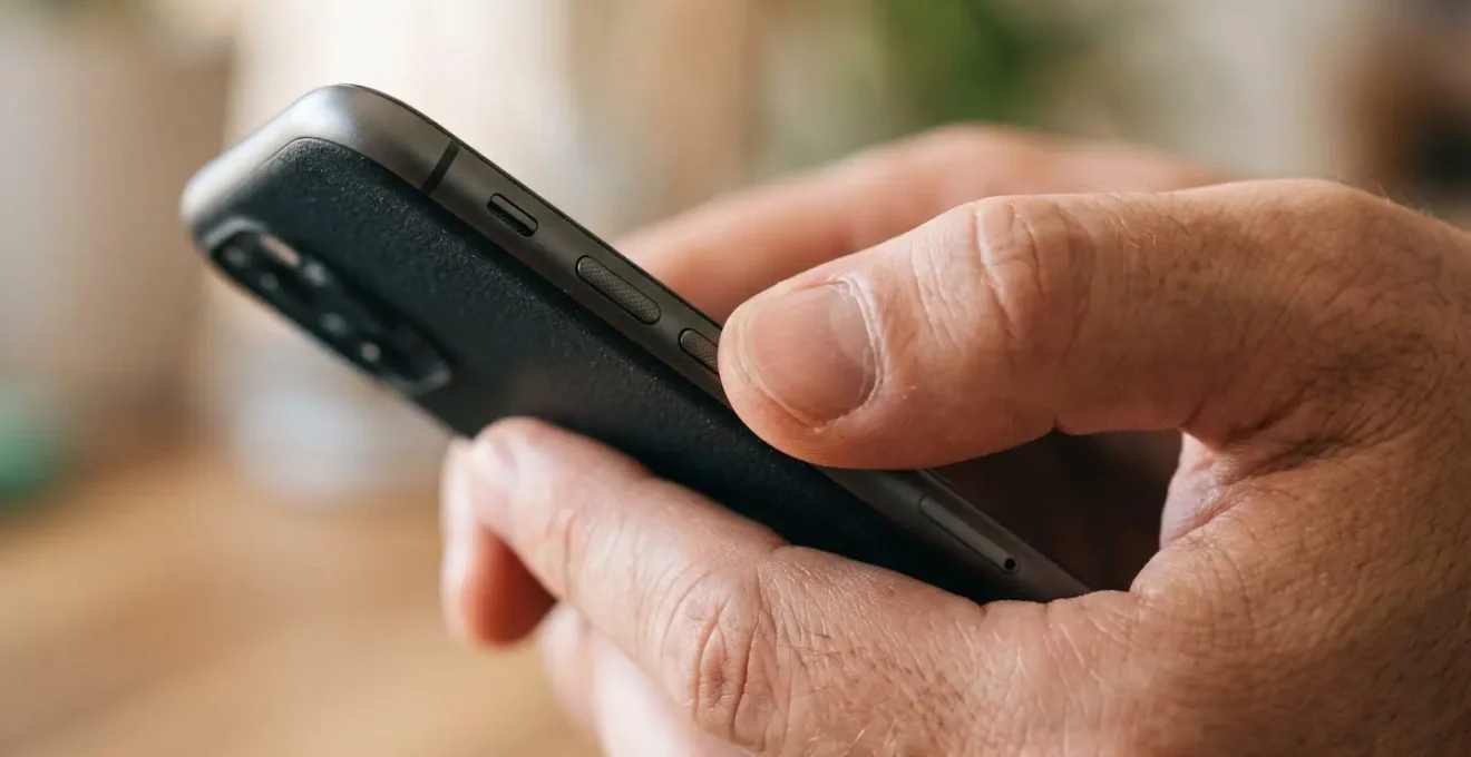 Main tenant un téléphone dans un environnement quotidien évoquant la facilité d'un paiement entre amis