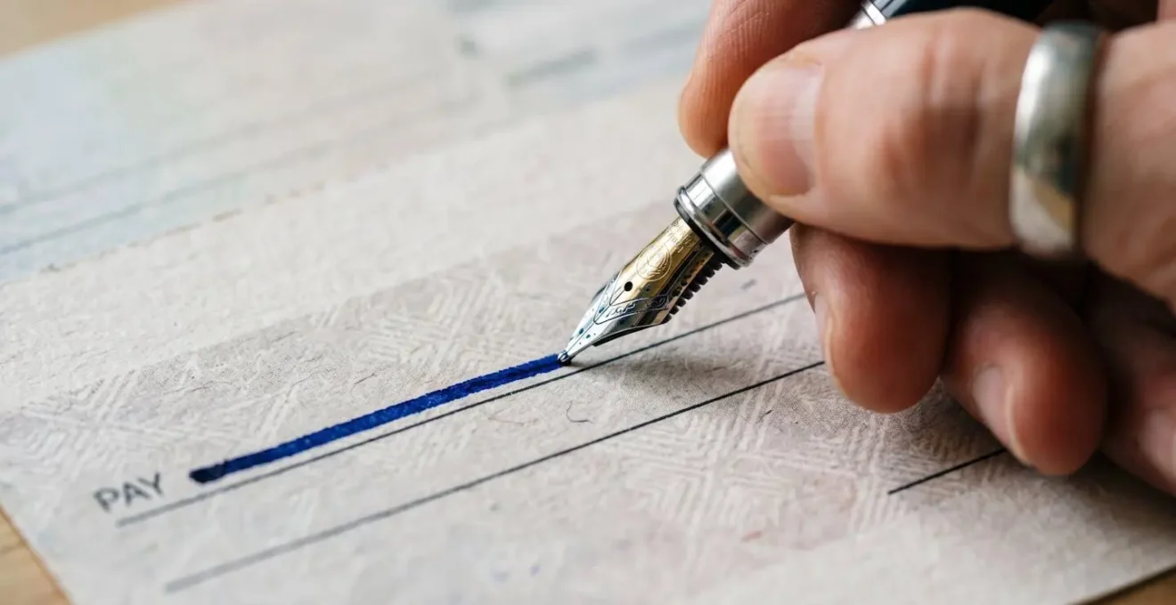 Gros plan sur un chèque bancaire en train d'être rempli avec un stylo, montrant les détails de sécurité anti-fraude